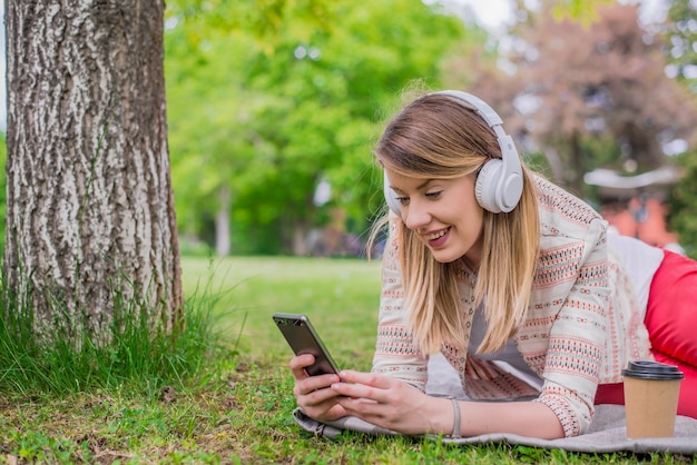 Free photo relaxed woman listening to the music with headphones lying on the grass. beautiful young woman with headphones enjoys in music while lying down in nature,enjoy music