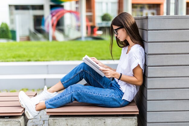 Relaxed woman reading a hard cover book at sunset sitting on a bench