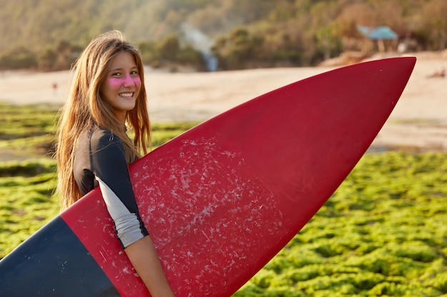 Relaxed woman with surf zinc on face, carries surfboard