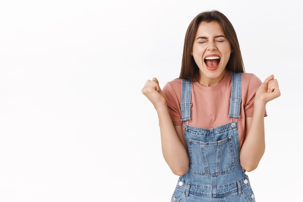 Relieved and happy attractive woman rejoicing, shouting yes joyfully clenching fists, achieve success, become champion or winner, close eyes triumphing, win lottery, white background