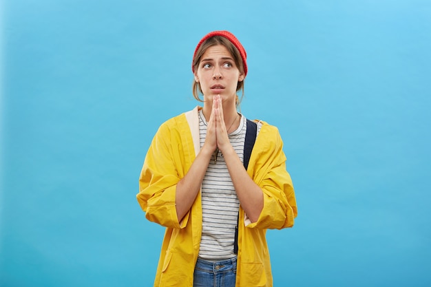 Religious wife in casual wear keeping her palms together praying for wellness of her husband who came hunting in dangerous place. Young pretty housewife asking for everything good at her life