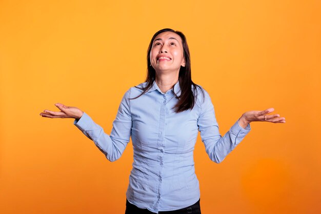 Religious woman prayer standing with palms faced to sky asking god for help, begging for forgiveness and peace in studio over yellow background. Spiritual asian woman expressing hope and belief.