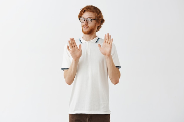 Free photo reluctant bearded redhead guy posing against the white wall with glasses