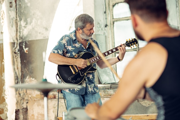 Repetition of rock music band. Electric guitar player and drummer behind the drum set.