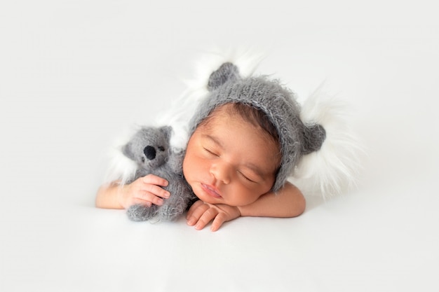 Resting newborn in little cute grey hat and with grey toy bear in his hands