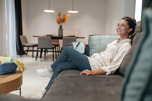 Resting. Smiling young woman sitting at home on the sofa