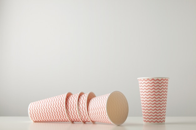 Free photo retail set of three paper cups decorated with red lines pattern felt down and one standing near isolated on white table