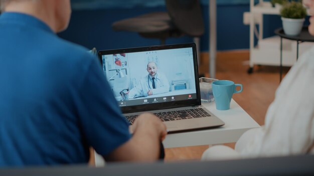 Retired couple doing online consultation on video call with medic. Elderly people using laptop to meet with doctor on video teleconference, talking about health care on telemedicine.