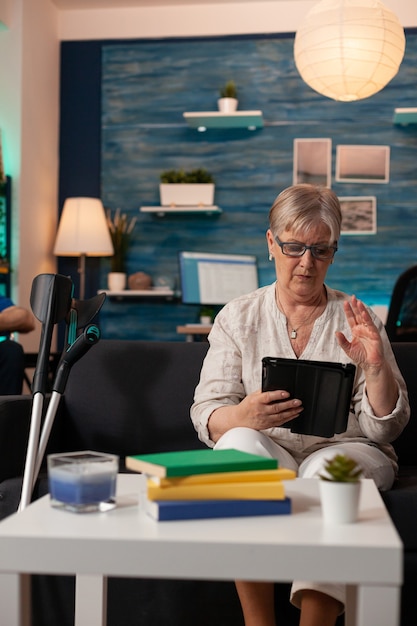 Retired woman waving at video call camera on tablet