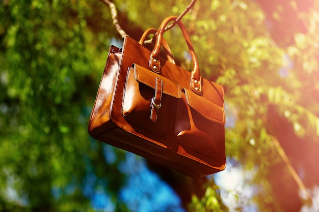 Retro brown  man leather bag  in bright colorful summer park hanging on leafes