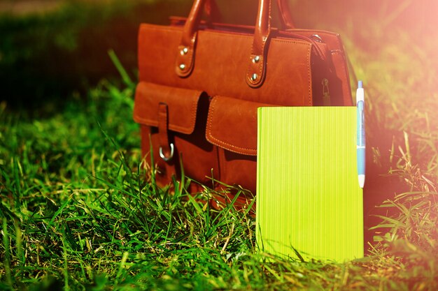 Retro brown  man leather bag and notebook in bright colorful summer grass in the park