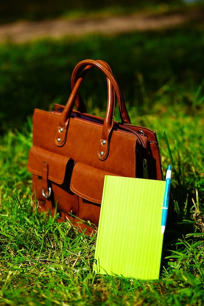 Free Photo retro brown  man leather bag and notebook in bright colorful summer grass in the park