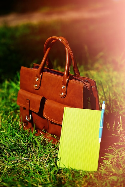 Free Photo retro brown  man leather bag and notebook in bright colorful summer grass in the park