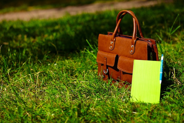 Retro brown  man leather bag and notebook in bright colorful summer grass in the park