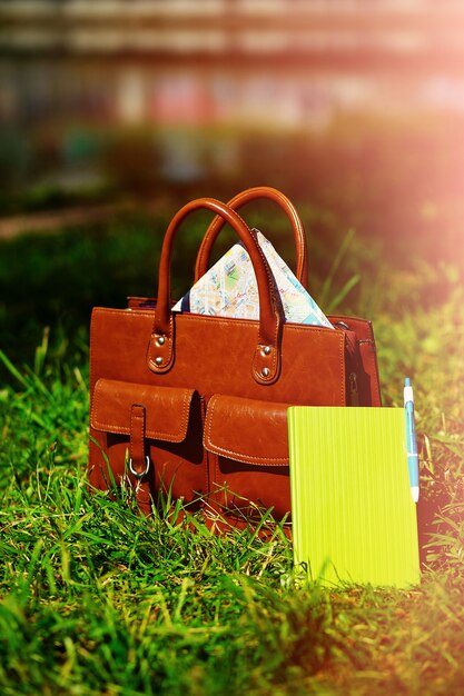 Retro brown  man leather bag and notebook in bright colorful summer grass in the park