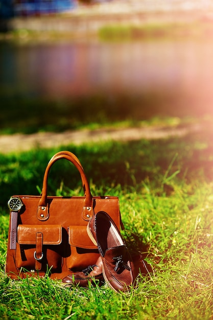 Retro brown shoes and man leather bag in bright colorful summer grass in the park