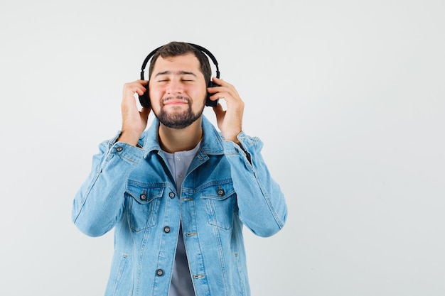 Retro-style man listening music with earphones in jacket,t-shirt and looking calm. front view. space for text