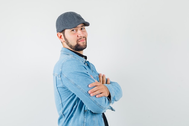 Retro-style man standing with crossed arms in jacket,cap and looking assured , front view.