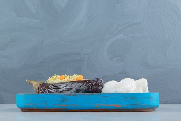 Rice in eggplant next to cross shaped radish on the board , on the marble.