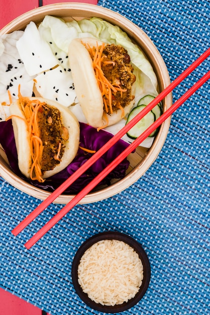 Free photo rice grain bowl with gua bao and salad in the bamboo steamer on placemat