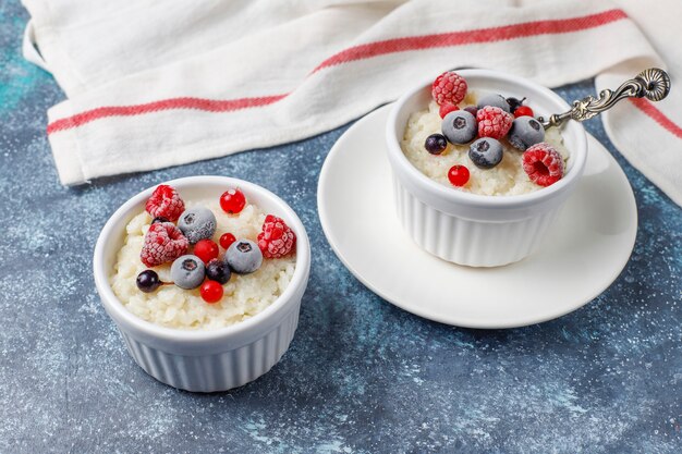 Rice pudding with frozen blueberries and raspberries in white bowl