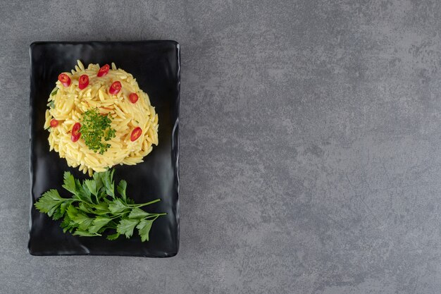 Rice with pepper slices and greens on black plate. High quality photo