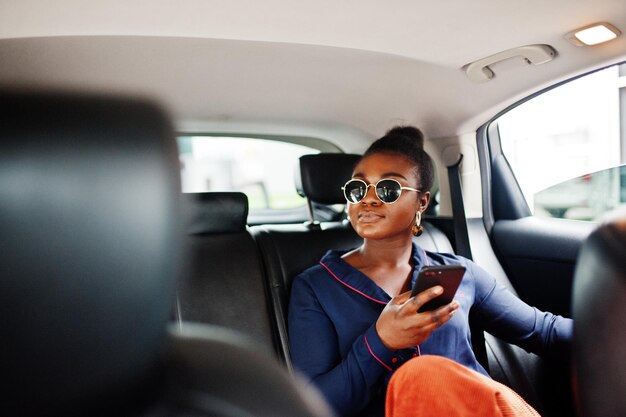 Rich business african woman on sunglasses sit at suv car with black leather seats Mobile phone at hand