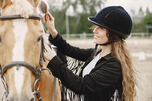 Free photo rider woman comb her horse on a ranch. woman has long hair and black clothes. female equestrian touching her brown horse.