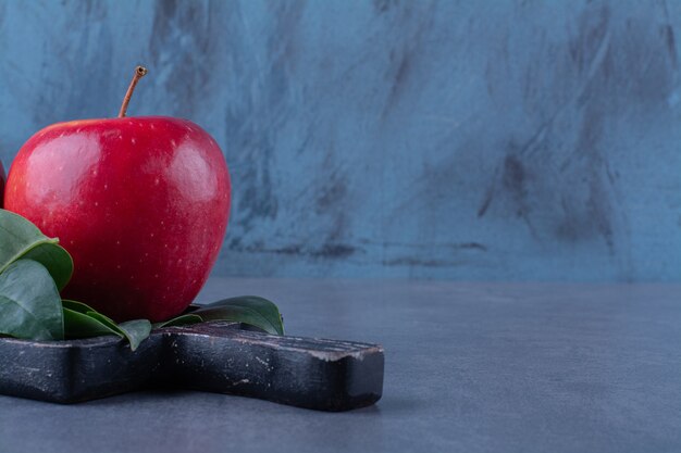 Ripe apples with leaves on board on marble table.