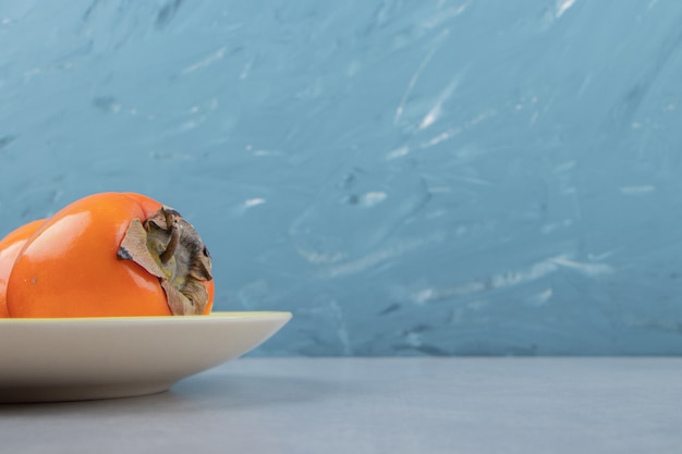 Ripe delicious persimmons on yellow plate. 