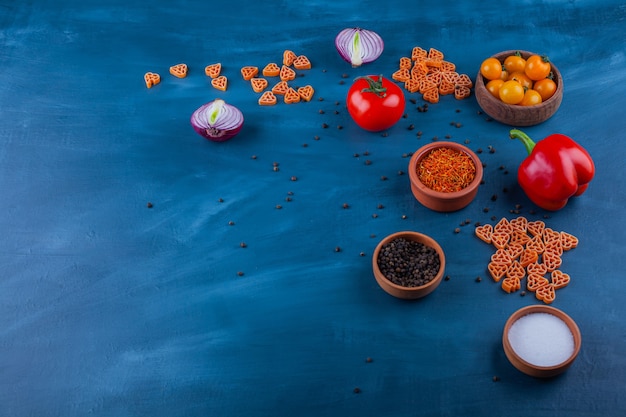 Ripe fresh vegetables and various condiments on blue surface.