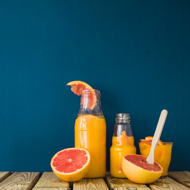 Free Photo ripe grapefruits with glass and bottles of juice on wooden table