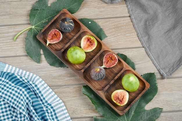 Free photo ripe green and black figs on wooden platter with a leaf and tablecloths.