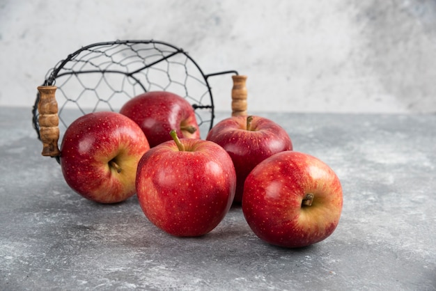 Ripe organic red apples out of metal basket on marble table.