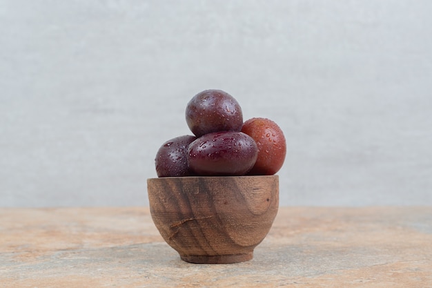 Ripe purple plums in bowl on marble background. 