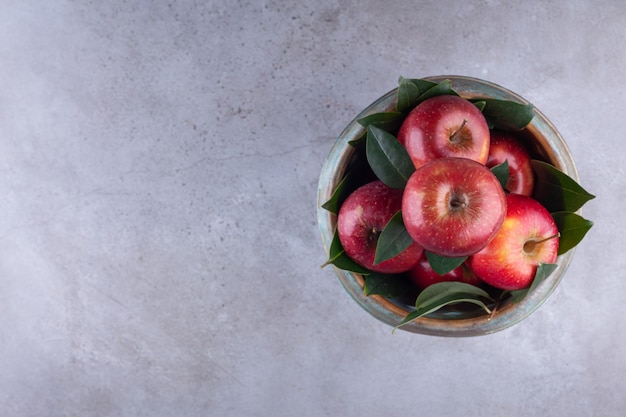 Ripe red apples with leaves in a bowl placed on a stone background . 