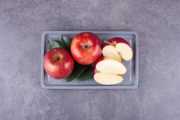 Ripe red apples with leaves placed on a stone surface .