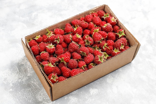 Ripe sweet raspberries in box on grey concrete . Close up, top view