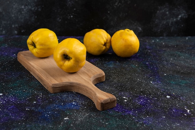 Free photo ripe whole quince fruits on wooden board and on dark table.