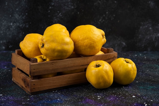 Ripe whole quince fruits in wooden box on dark table. 