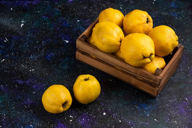 Ripe whole quince fruits in wooden box on dark table. 