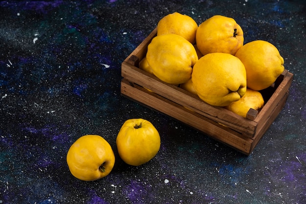 Ripe whole quince fruits in wooden box on dark table. 