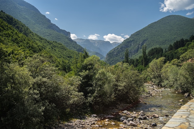 River surrounded by hills covered in greenery under a cloudy sky and sunlight