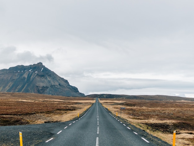 Free photo road surrounded by hills covered in greenery and snow under a cloudy sky in iceland