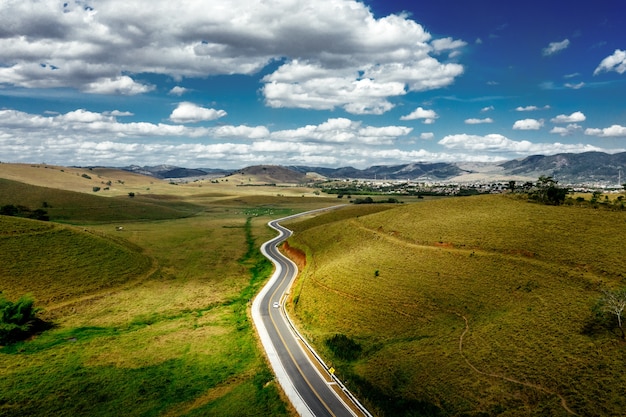 Free photo road surrounded by hills covered in greenery with mountains under a cloudy sky