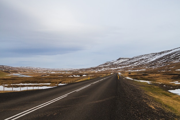 Free Photo road surrounded by hills covered in the snow and greenery under a cloudy sky in iceland