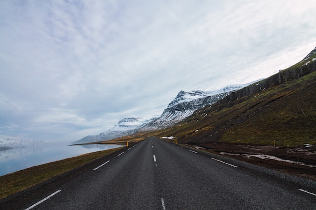 Free Photo road surrounded by the river and hills covered in the snow and grass under a cloudy sky in iceland