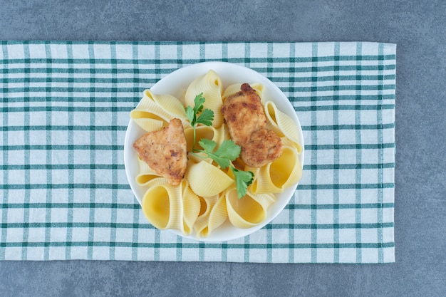 Roasted chicken nuggets and boiled pasta in white bowl.