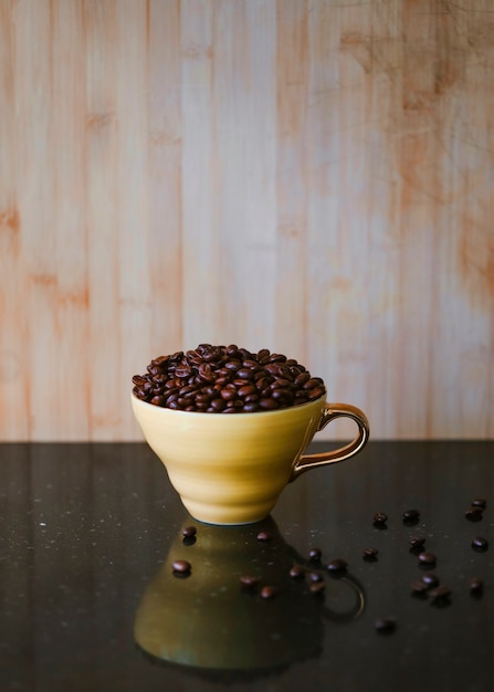 Roasted coffee beans in brown ceramic cup on reflective desk