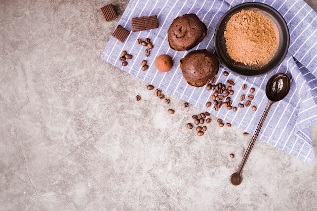 Free Photo roasted coffee beans; chocolate pieces; and cupcake on napkin over old backdrop